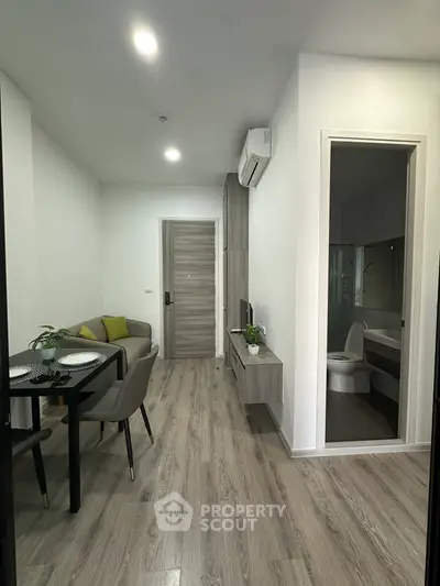 Modern apartment interior with open living and dining area, featuring sleek furniture and wood flooring.