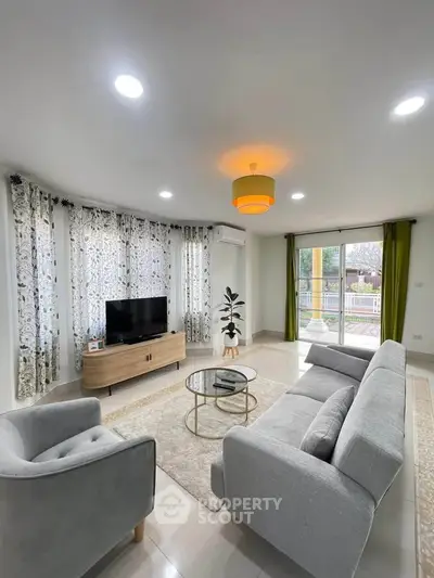 Spacious living room with modern decor and large windows offering natural light and garden view.