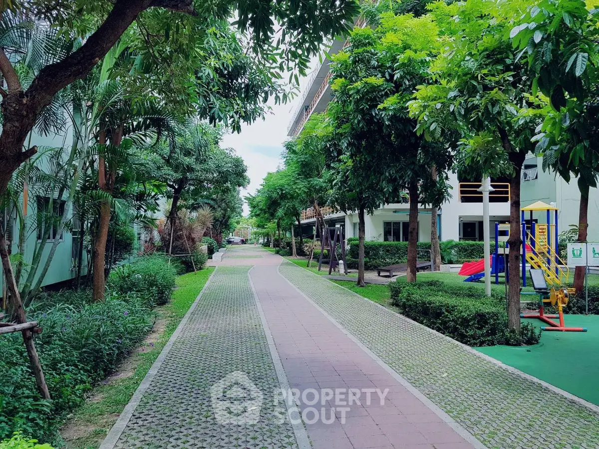 Beautiful garden pathway with lush greenery and playground in residential complex.