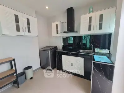 Modern kitchen with sleek black countertops and white cabinets, featuring a washing machine and ample storage space.