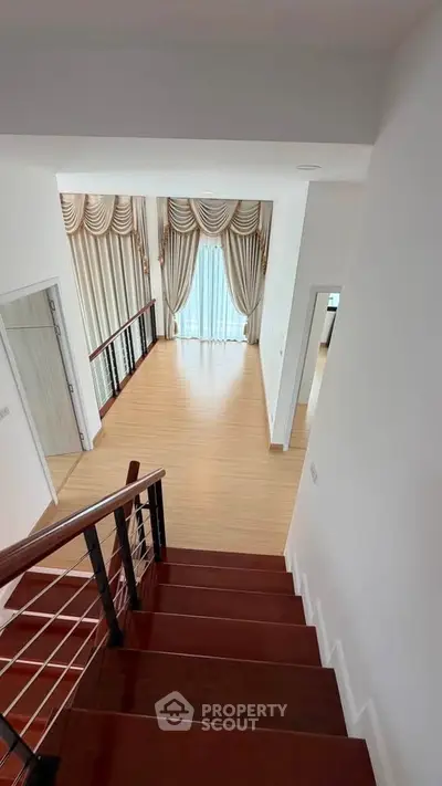 Elegant staircase leading to a bright living area with luxurious curtains and wooden flooring.