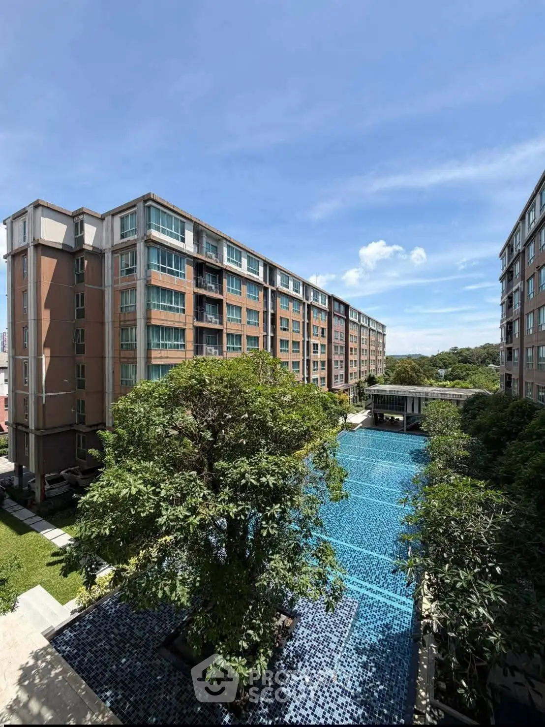 Stunning residential complex with a sparkling pool and lush greenery under a clear blue sky.