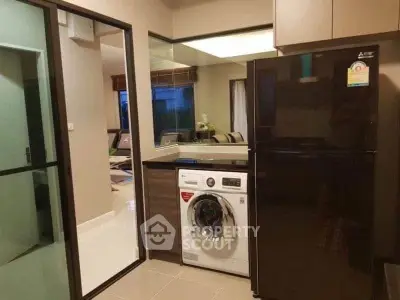 Modern kitchen with sleek appliances including washing machine and fridge, open layout to living area.