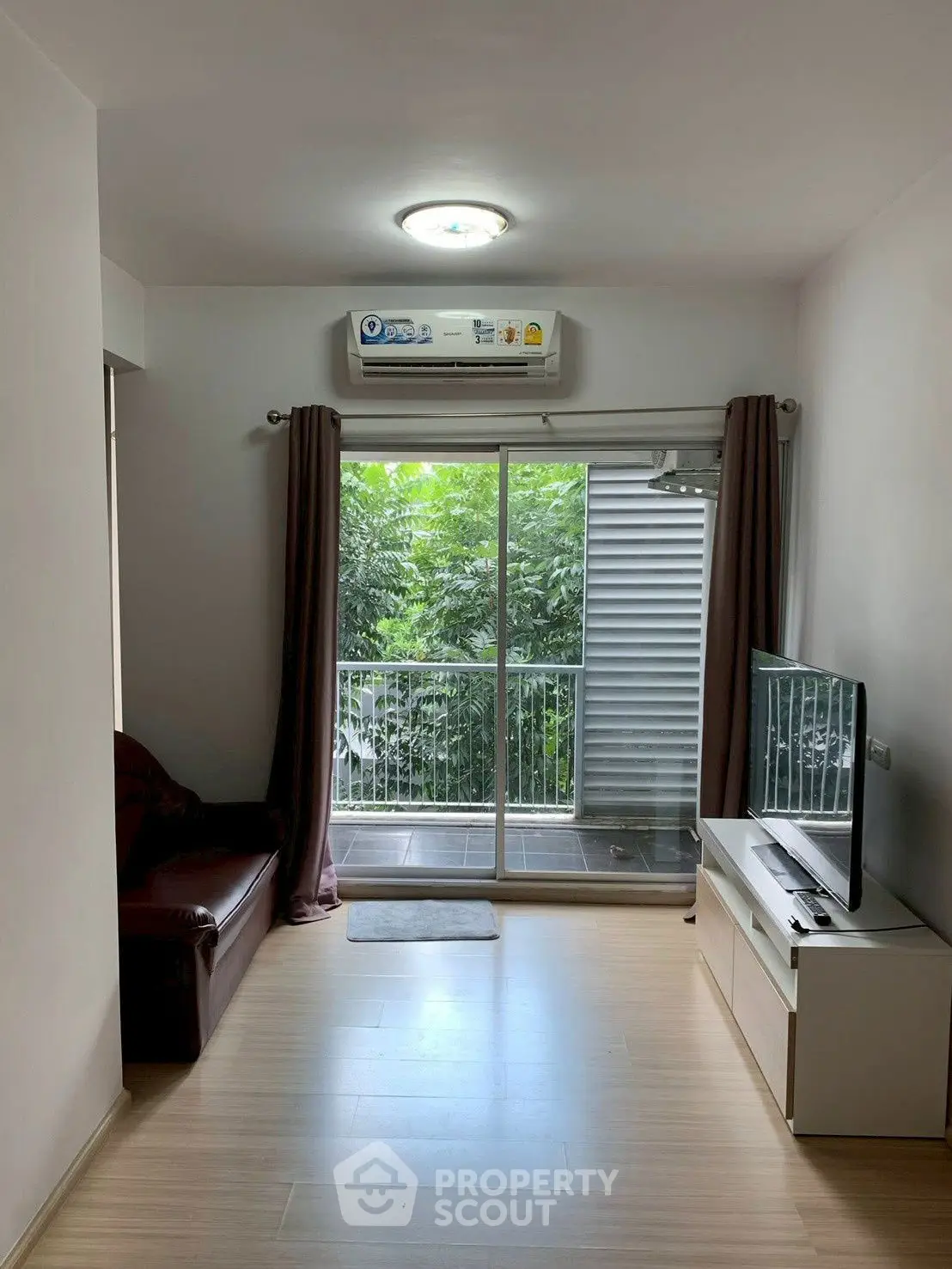 Modern living room with balcony view and natural light, featuring sleek furniture and air conditioning.