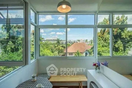 Charming breakfast nook with panoramic window views of lush greenery and rooftops.