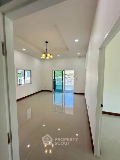 Spacious living room with glossy tiled floors and modern lighting, opening to a bright outdoor view.