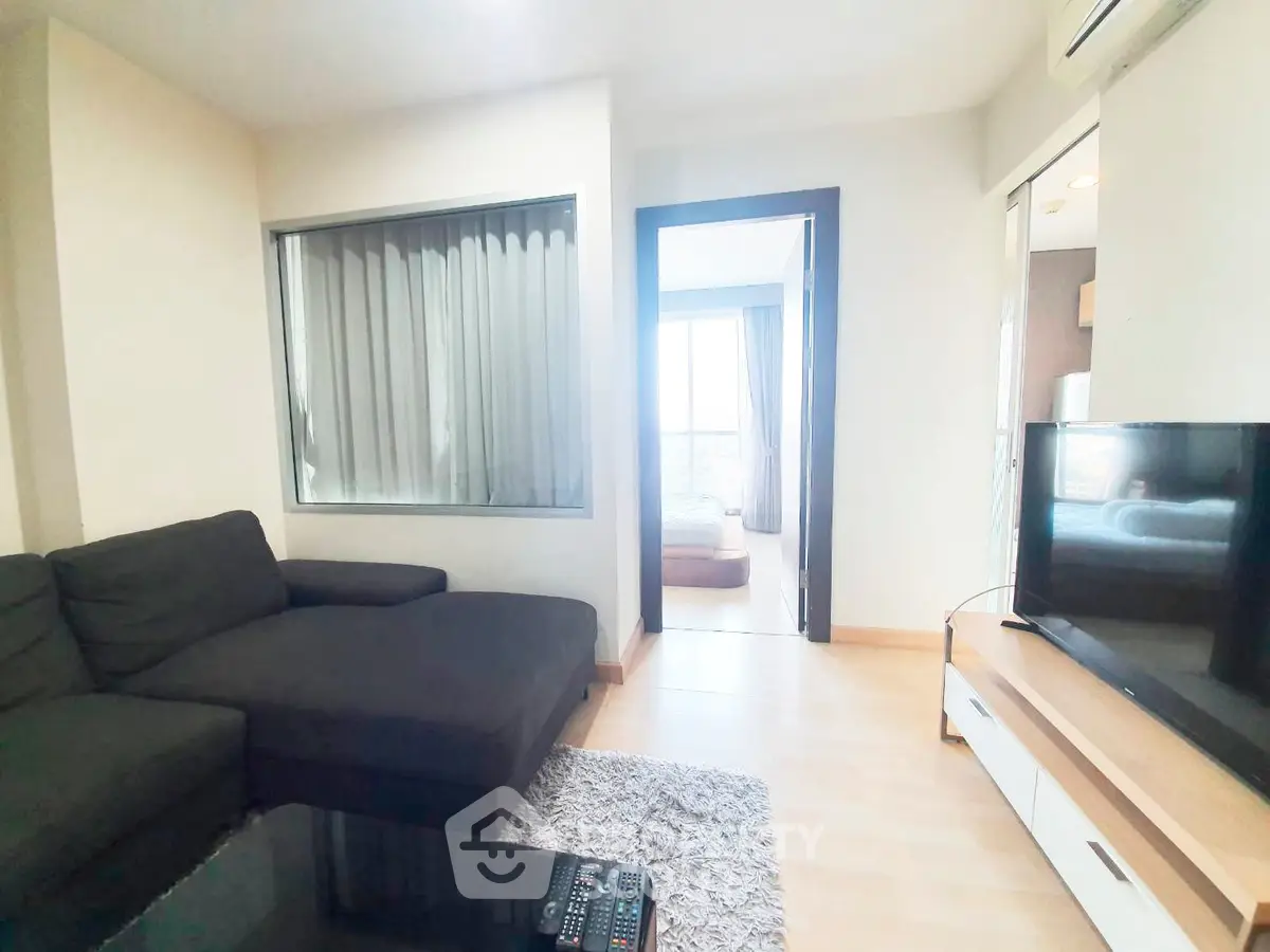 Modern living room with cozy sofa and TV, leading to a bright bedroom with balcony view.