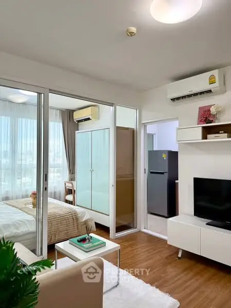 Modern open-plan living room with bedroom view, featuring sleek furniture and natural light.