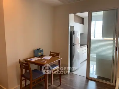 Modern dining area with wooden table and chairs adjacent to sleek kitchen with stainless steel fridge.