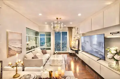 Luxurious living room with elegant decor and stunning city view, featuring a large TV and chandelier lighting.