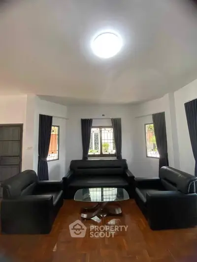 Spacious living room with modern black leather sofas and elegant wooden flooring.