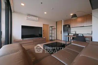 Modern living room with leather sofa, flat-screen TV, and open kitchen layout