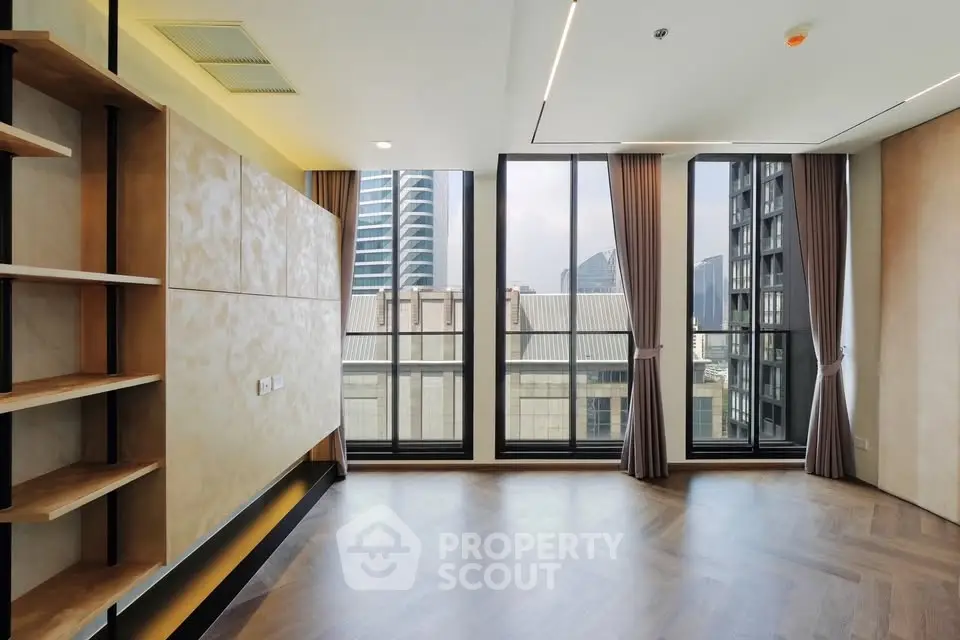 Spacious modern living room with large windows and city view, featuring elegant wooden flooring and built-in shelves.