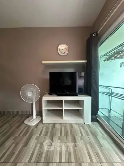 Modern living room with sleek TV stand and fan, adjacent to a large glass balcony door.
