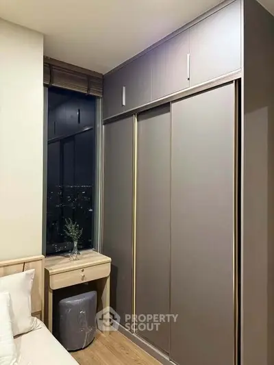 Modern bedroom with sleek wardrobe and night city view from window.