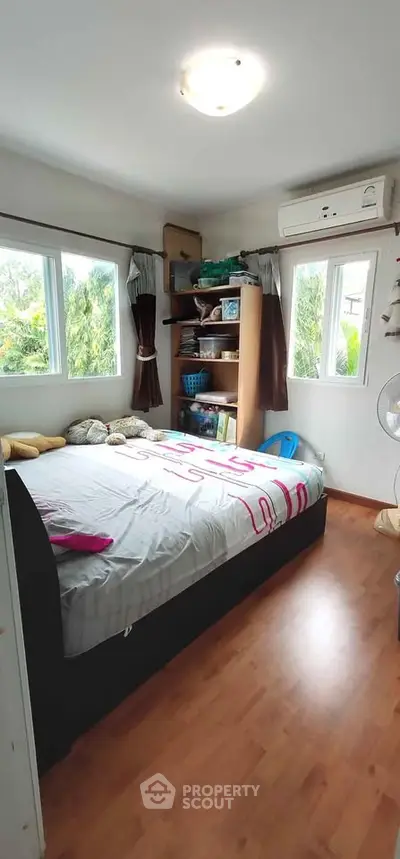 Cozy bedroom with large windows and wooden flooring, featuring a comfortable bed and ample natural light.