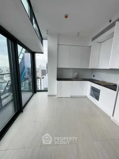 Modern kitchen with sleek white cabinets and stunning city view from large windows.