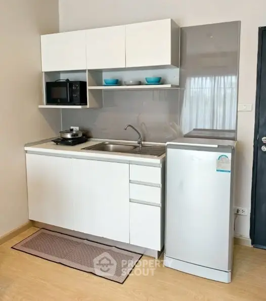 Compact modern kitchen with sleek white cabinets and appliances, ideal for small spaces.