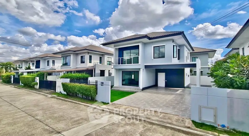 Modern suburban homes with lush greenery and spacious driveways under a vibrant sky.