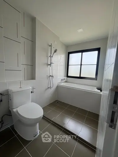 Modern bathroom with sleek tiles and a bathtub, featuring a large window for natural light.