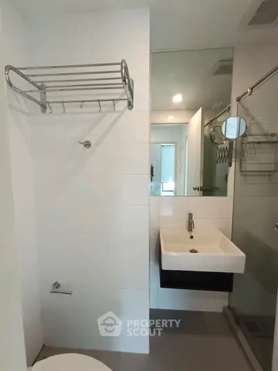 Modern bathroom with sleek fixtures and large mirror, featuring a wall-mounted sink and towel rack.