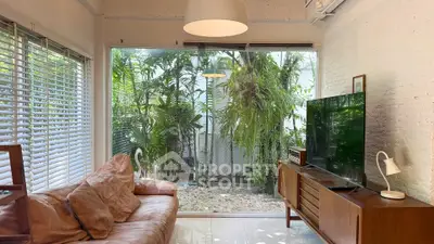 Charming living room with large window view of lush garden, cozy leather sofa, and modern decor.