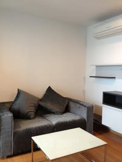 Modern living room with sleek sofa and minimalist decor, featuring air conditioning and wooden flooring.