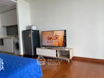 Modern studio apartment with wooden flooring, compact kitchen, and cozy living area featuring a TV and mini fridge.