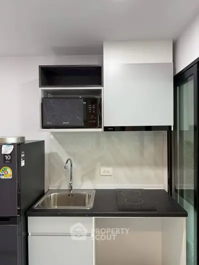 Modern compact kitchen with sleek black countertop, built-in microwave, and electric cooktop.