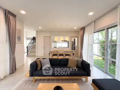 Modern living room with stylish furniture and large windows overlooking a garden, featuring elegant lighting and decor.