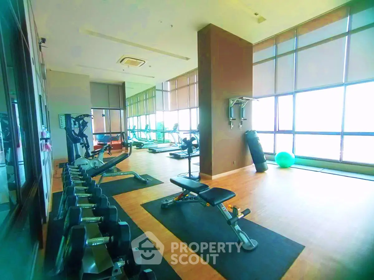 Spacious gym with modern equipment and large windows offering natural light.