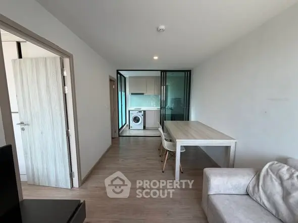 Modern apartment interior with open layout, featuring a dining area and kitchen with washing machine.