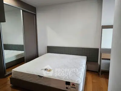 Modern bedroom with sleek design and comfortable mattress, featuring a mirrored wardrobe and wooden flooring.