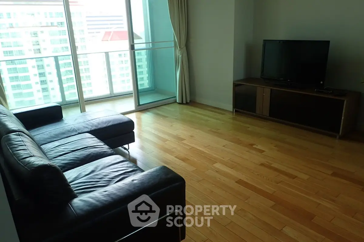 Spacious living room with wooden flooring and large windows offering city views.