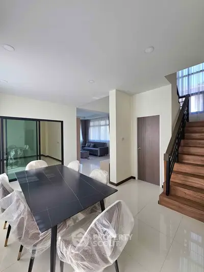 Modern open-plan living and dining area with sleek staircase and natural light.