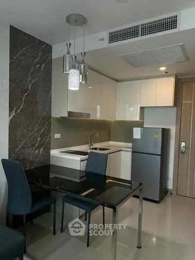 Modern kitchen with sleek design, featuring a glass dining table and contemporary lighting.