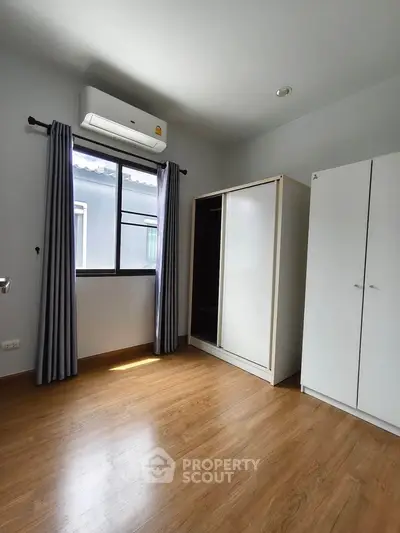 Spacious bedroom with wooden flooring and ample natural light, featuring a modern wardrobe and air conditioning.