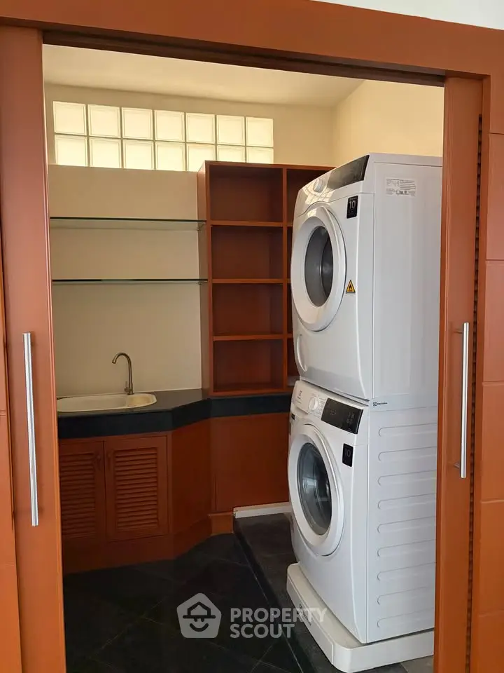 Compact laundry room with stacked washer and dryer, sleek cabinetry, and a utility sink.