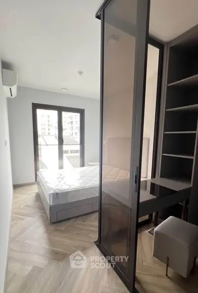 Modern bedroom with sliding glass door and built-in shelving, featuring a stylish bed and natural light.