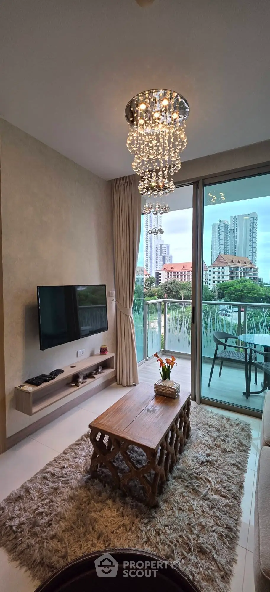 Stylish living room with modern chandelier and balcony view in a high-rise apartment.