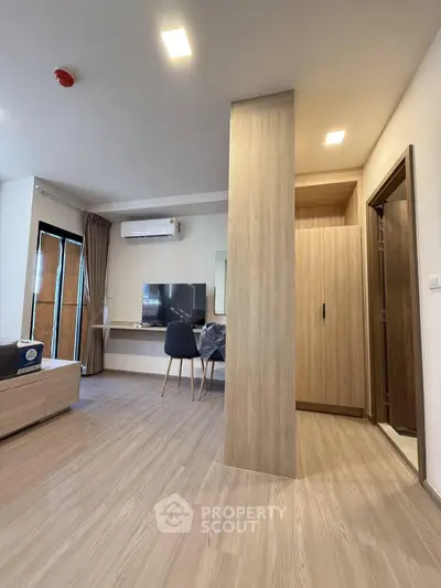 Modern living room with sleek wooden flooring and stylish furniture, featuring a wall-mounted TV and air conditioning.