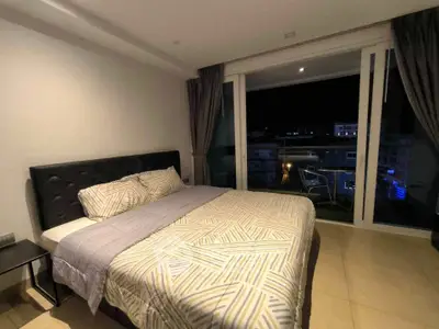 Modern bedroom with large window and night city view, featuring stylish bedding and cozy ambiance.