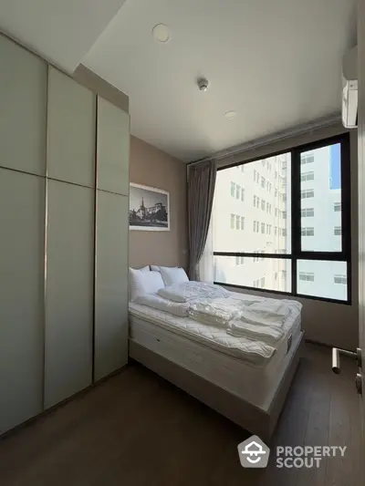 Modern bedroom with large window and built-in wardrobe in urban apartment