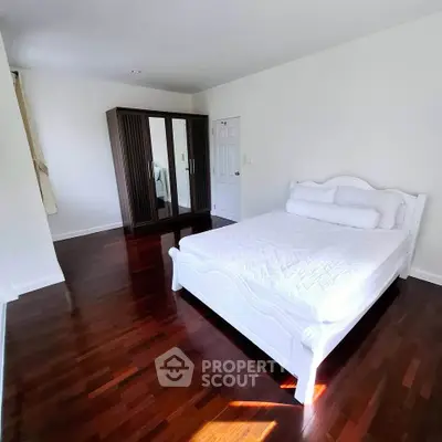 Spacious bedroom with elegant white bed and wooden wardrobe, featuring polished hardwood floors.