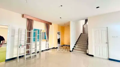 Spacious living room with modern staircase and elegant curtains in a bright, open layout.