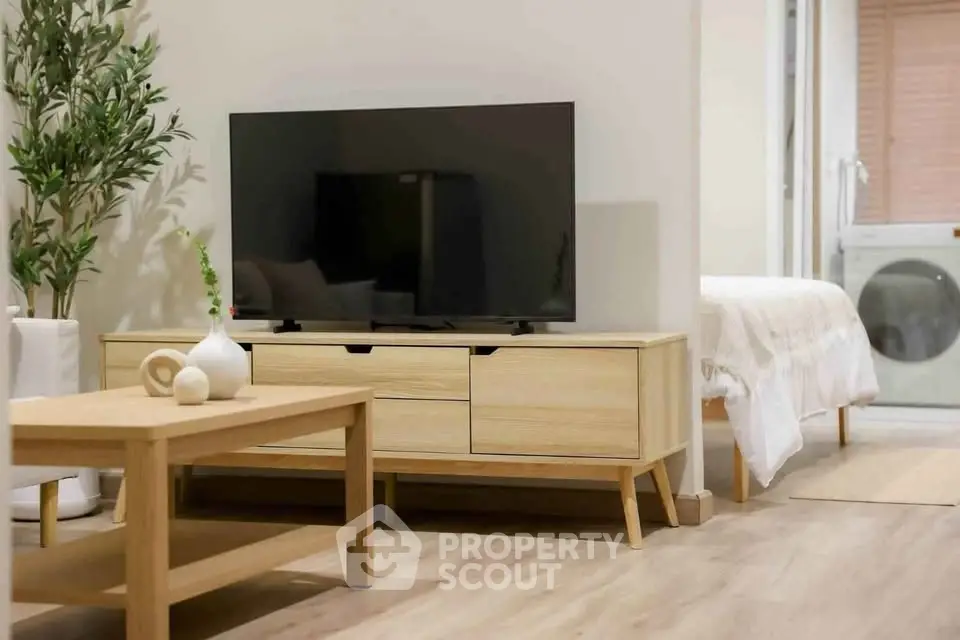 Modern living room with sleek wooden furniture and a flat-screen TV, leading to a cozy bedroom.