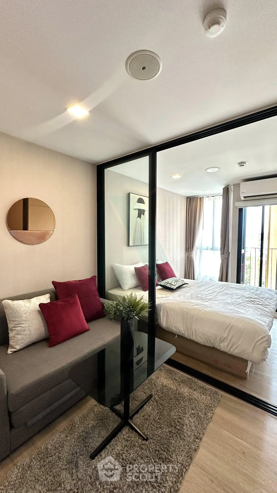 Modern apartment with cozy living room and stylish bedroom separated by glass wall.
