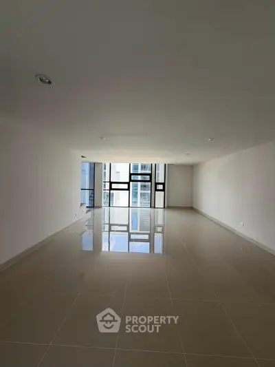 Spacious modern living room with large windows and glossy tiled floors in a contemporary apartment.