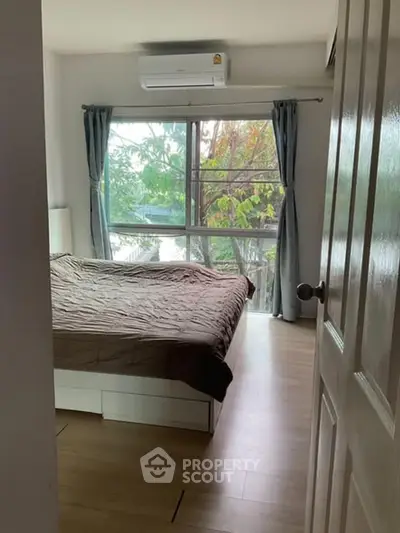 Cozy bedroom with large window and natural light, featuring a comfortable bed and air conditioning.