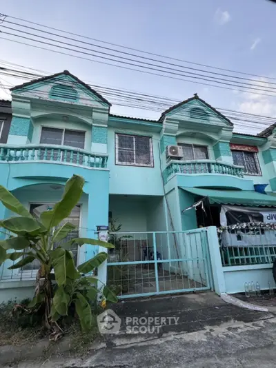 Charming turquoise townhouse with balcony and gated entrance in a serene neighborhood.